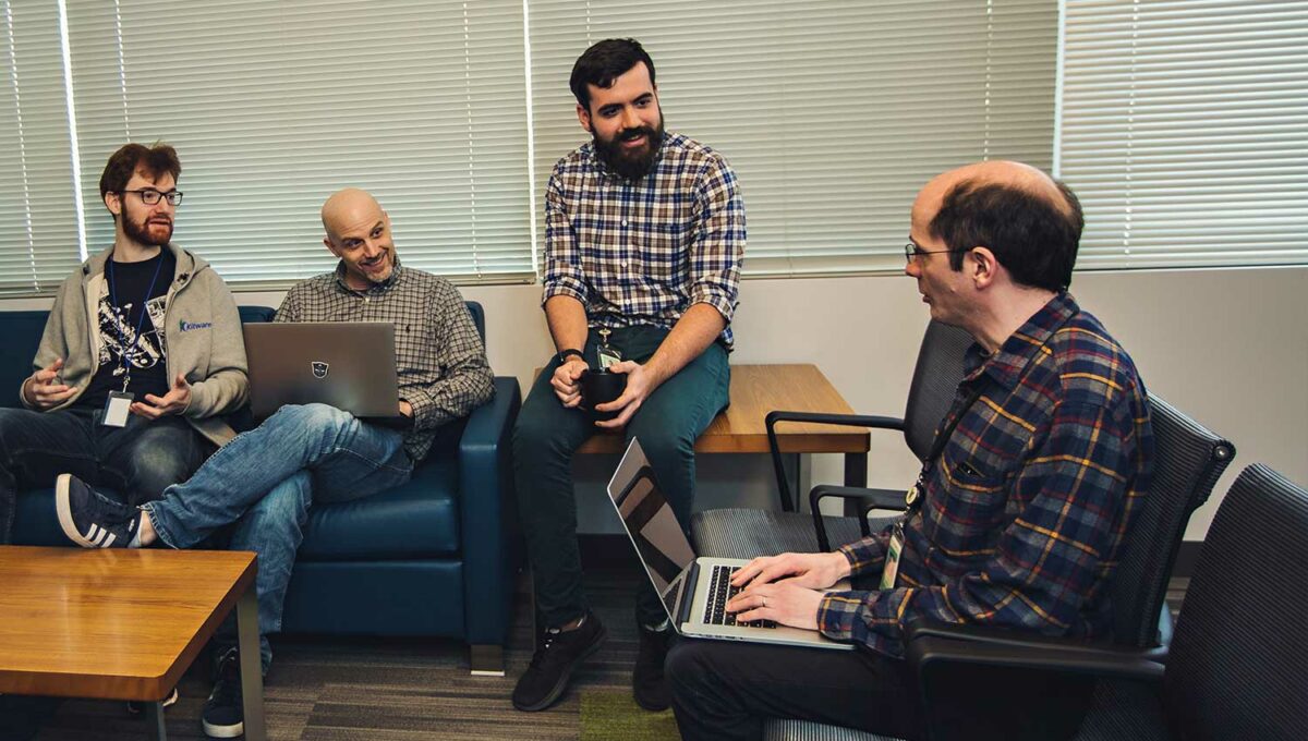 four people discussing a project with laptops on laps