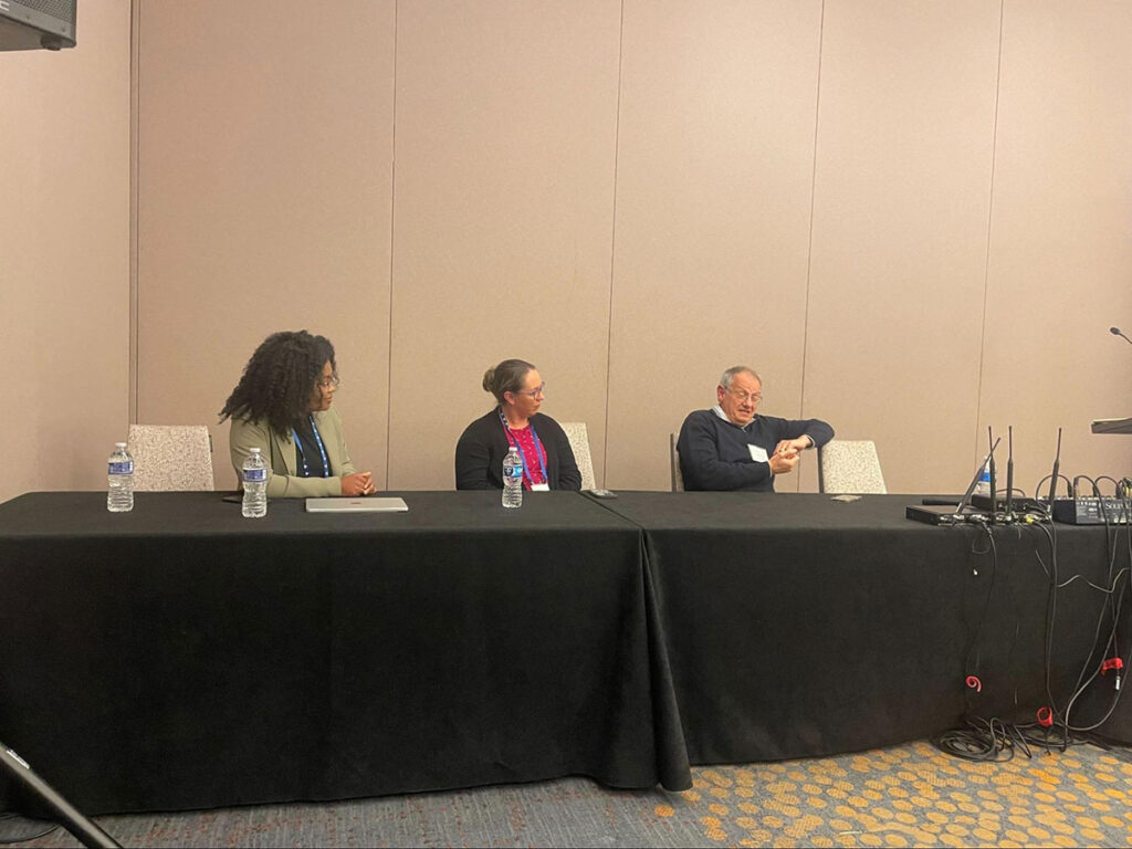 3 people at a table in front of a conference room of people