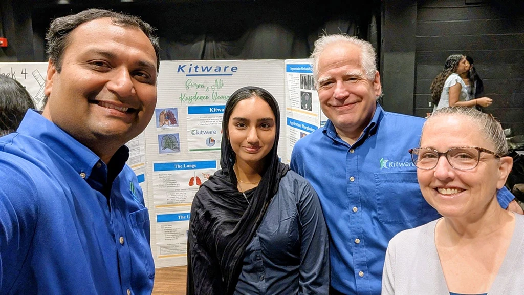 Four people posing for a selfie in front of a Kitware science presentation board about the lungs.