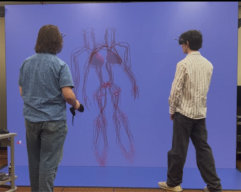 Two researchers wearing motion-tracking glasses view a large stereoscopic 3D projection of a human circulatory system in an immersive VR environment.