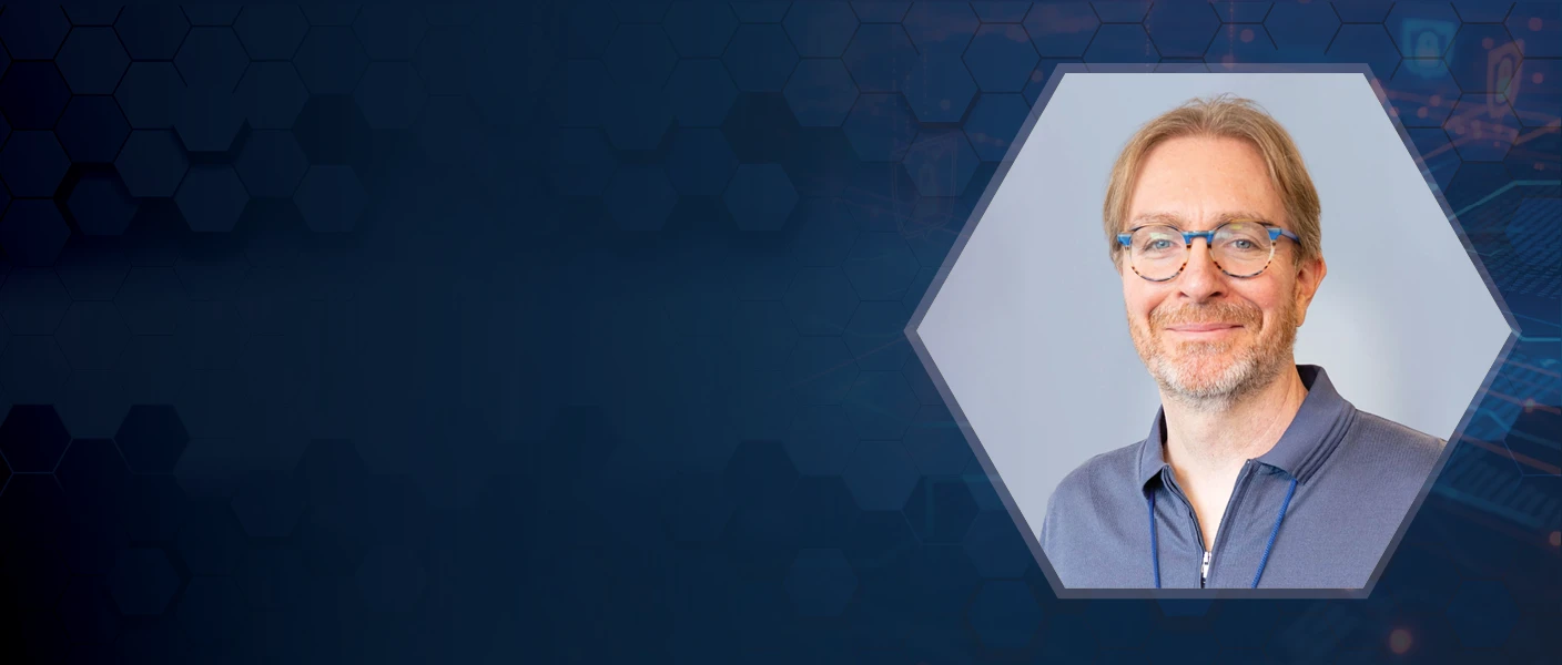 A cybersecurity spotlight hero banner featuring a hexagonal portrait of a smiling man with glasses against a dark navy background with honeycomb patterns and abstract network security icons.